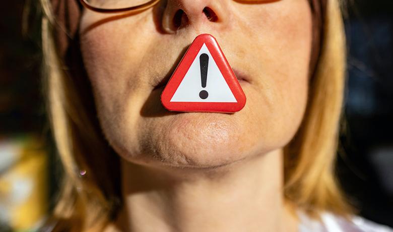 Primer pla de dona amb una petita senyal de trànsit amb un signe d'admiració sobre la boca