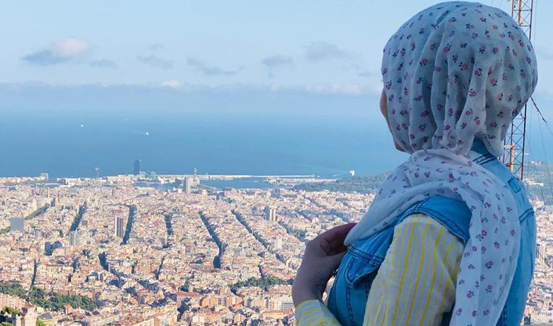 Una noia que porta hijab mira, d'esquena a càmera, les vistes de la ciutat de Barcelona
