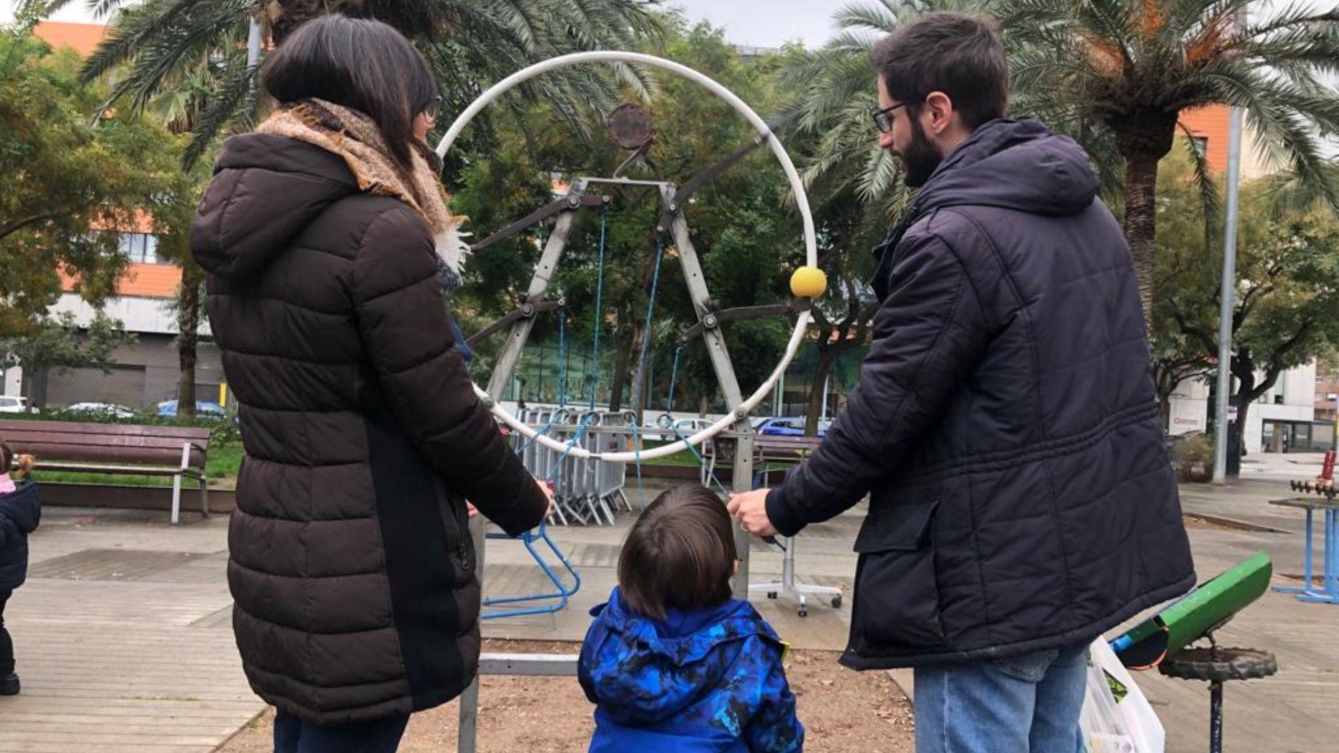 Un infant juga, amb dos adults, a un joc instal·lat al circuit de les joguines