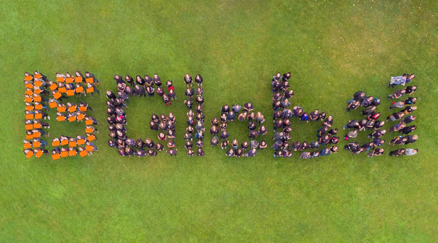 Presa aèria que mostra un grup de persones organitzades per formar la paraula "ISGlobal" sobre un camp de gespa verda.